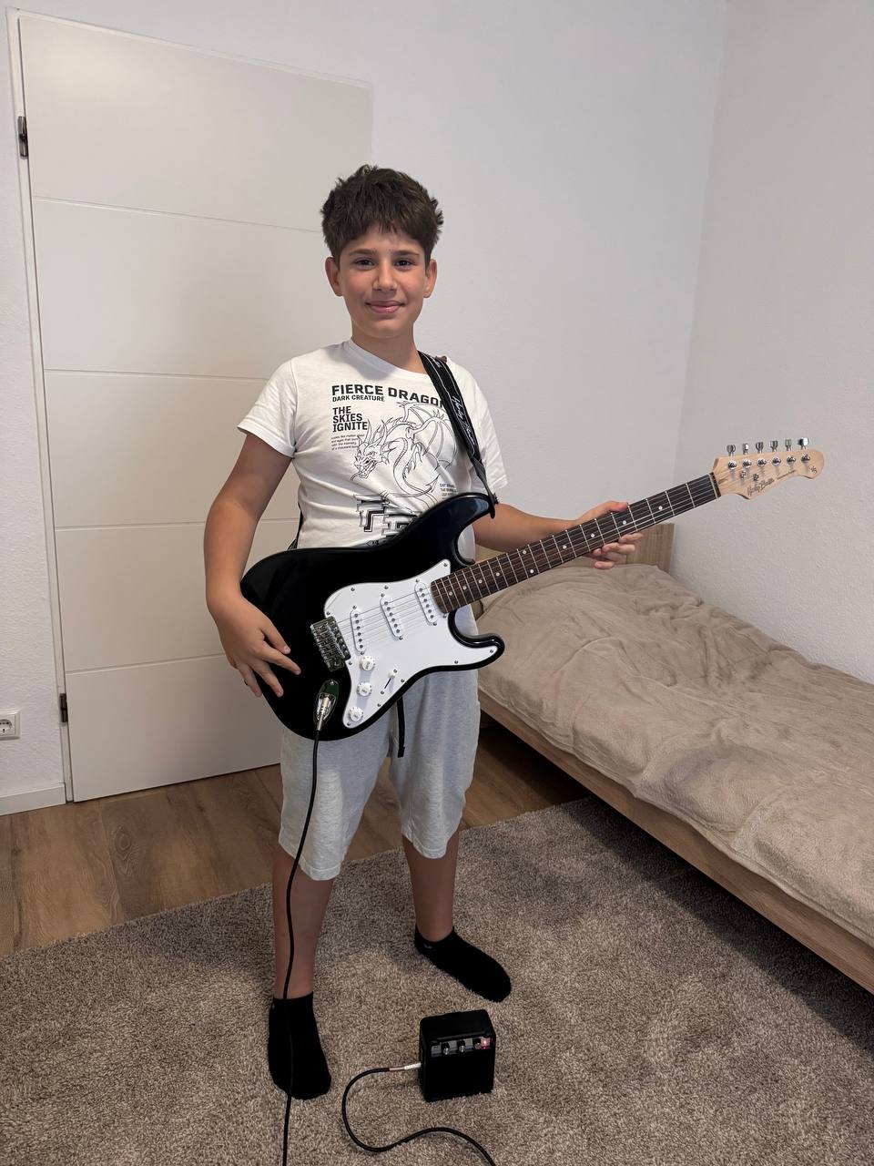 Ein Junge mit seiner neuen E-Gitarre und einem kleinen Verstärker