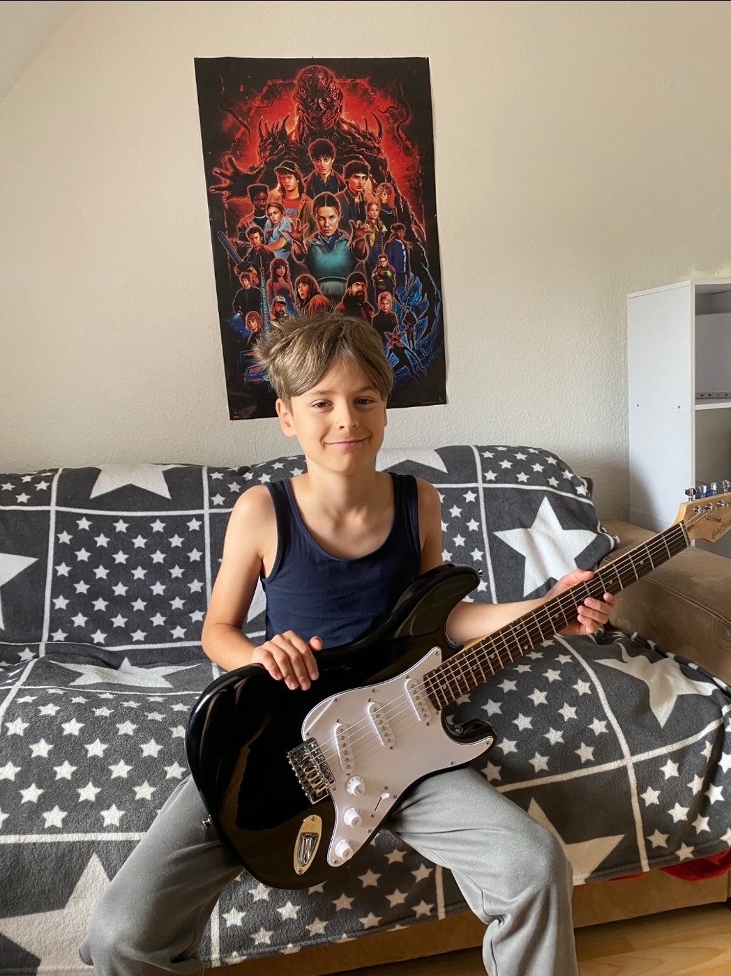 Ein Junge sitzt mit seiner neuen E-Gitarre auf dem Sofa